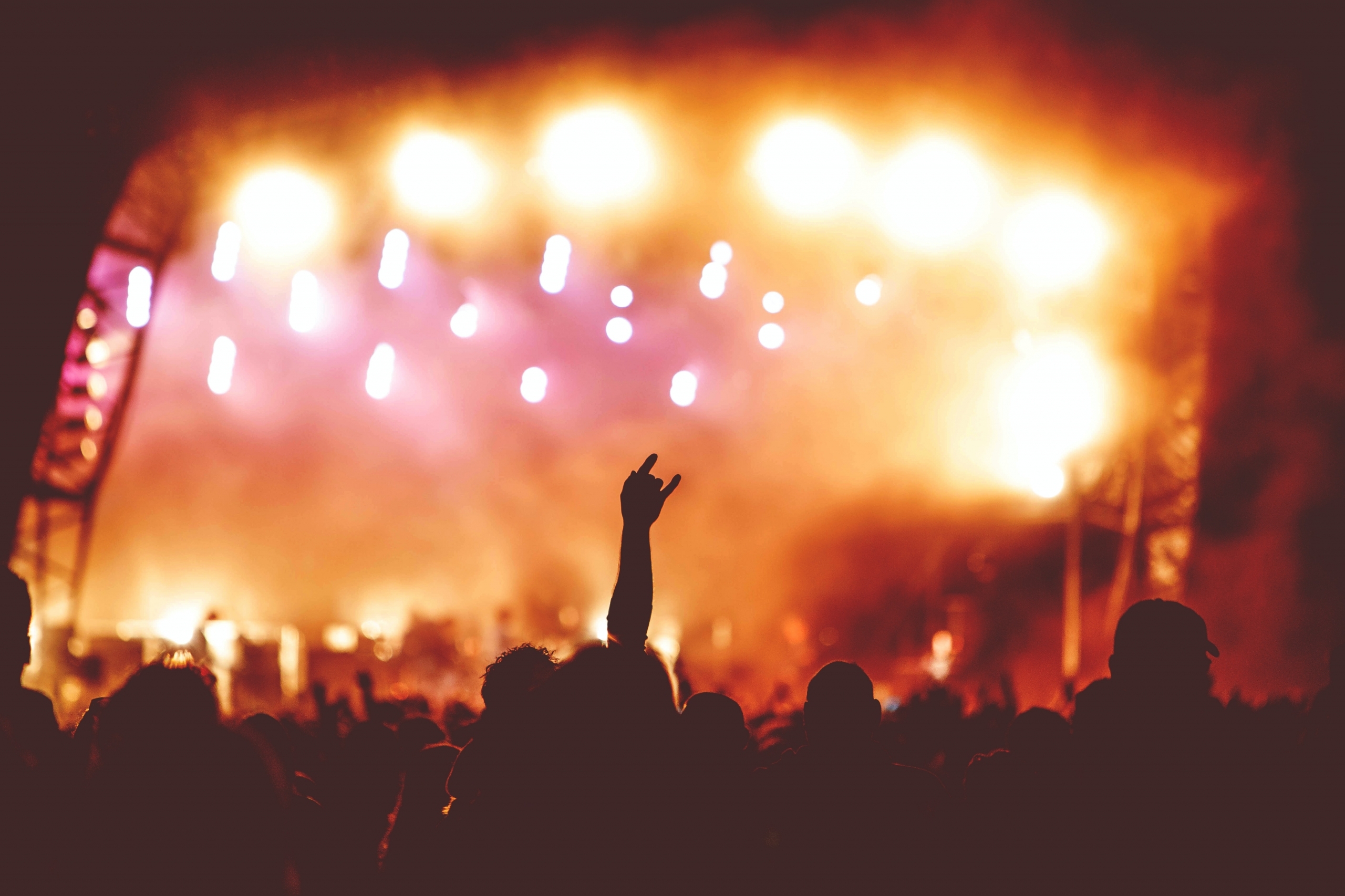 Image of an outdoor music event, showing a silhouette of the crowd against bright stage lights.