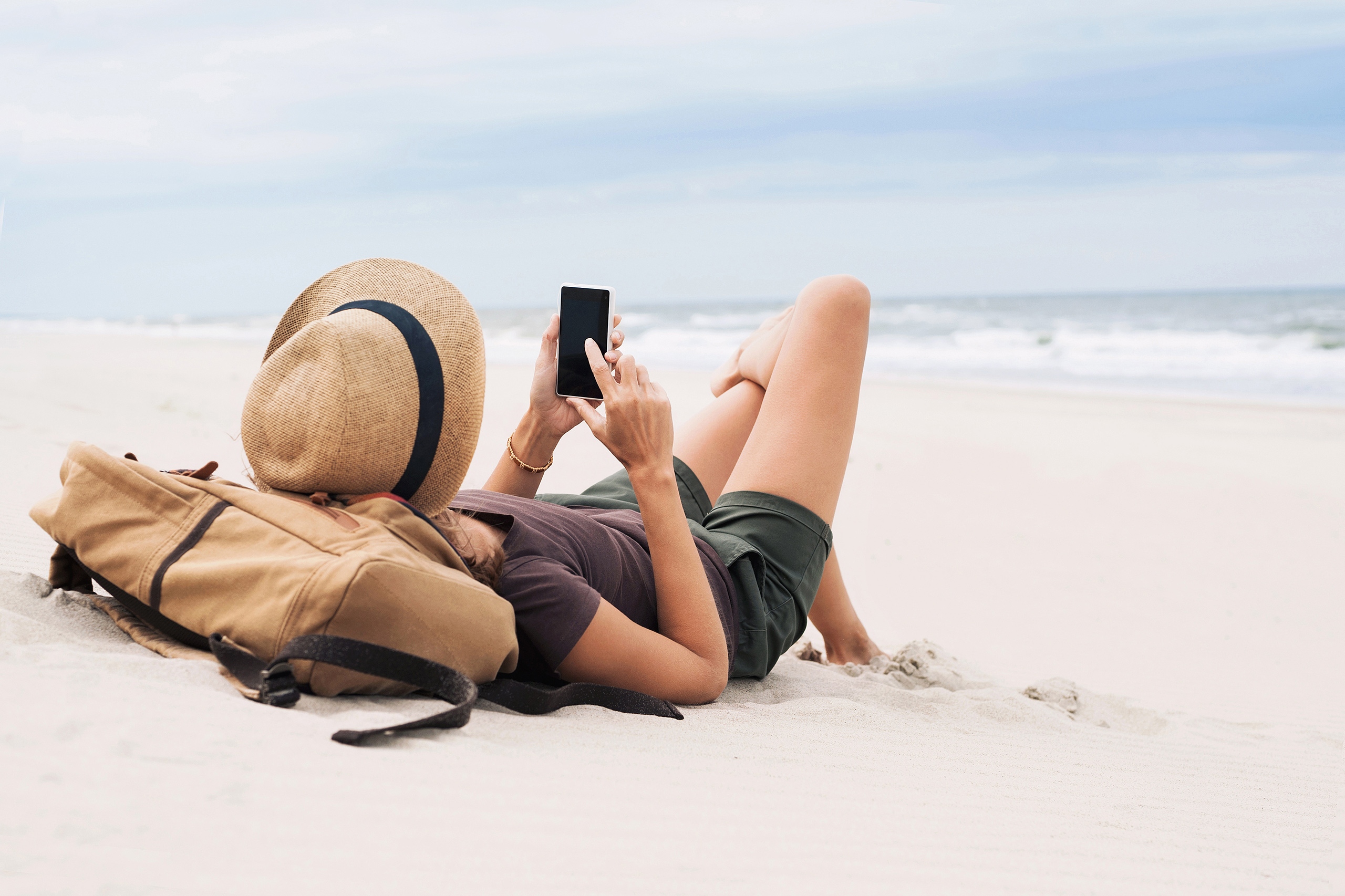 Image of a woman lying on a beach and looking at her phone