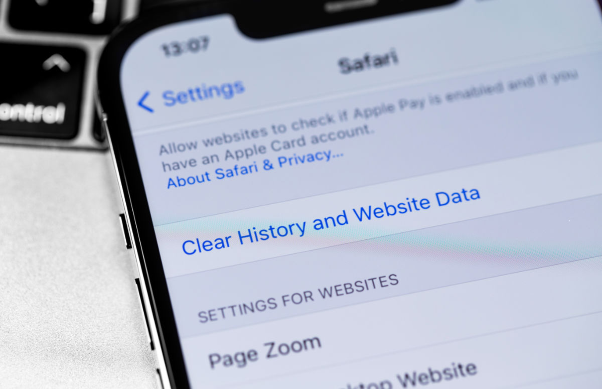 A close up of an iPhone with the Settings app open to the page displaying the option to clear history and website data for Safari