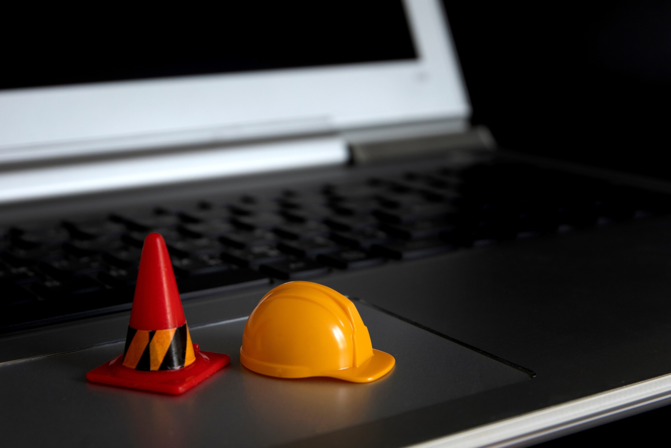 Laptop with a small model hard hat and traffic cone on the trackpad